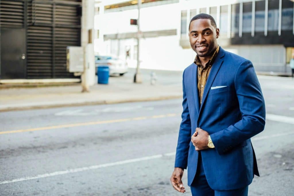 A man wearing a blue suit standing on the side of the street.