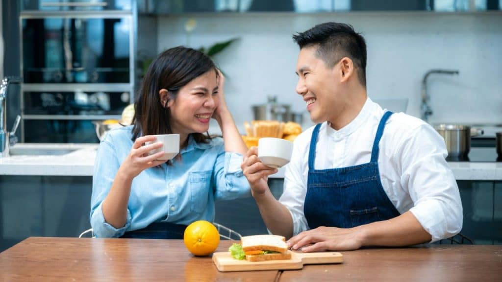 A smiling couple shares a meal and coffee in a modern, well-lit kitchen.