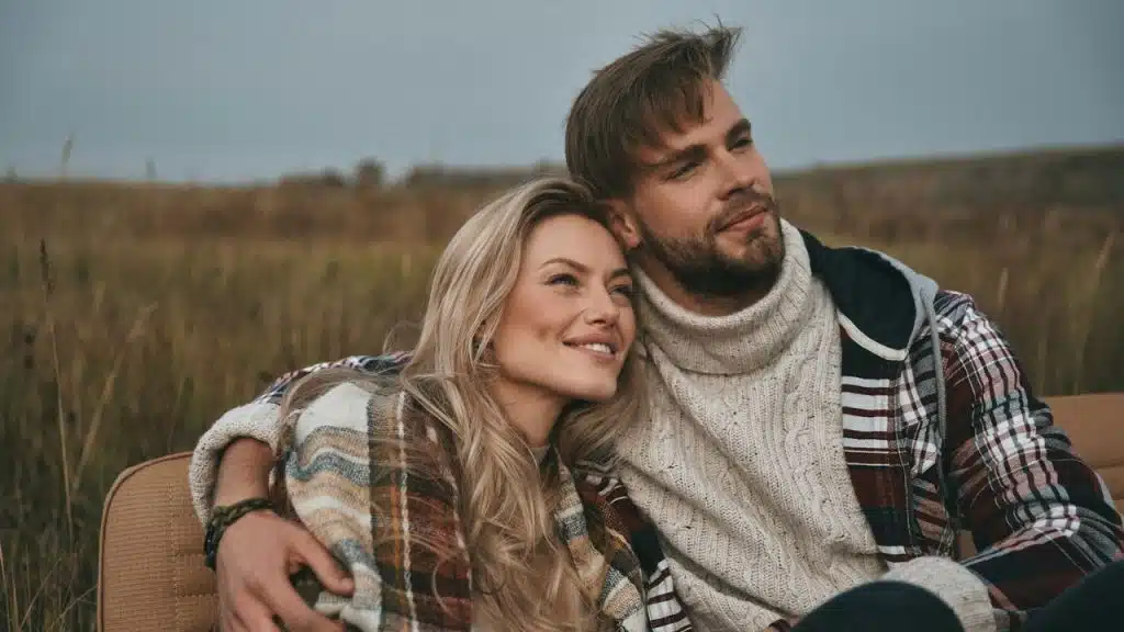 Couple embracing in a dry, grassy field while looking out at the landscape.