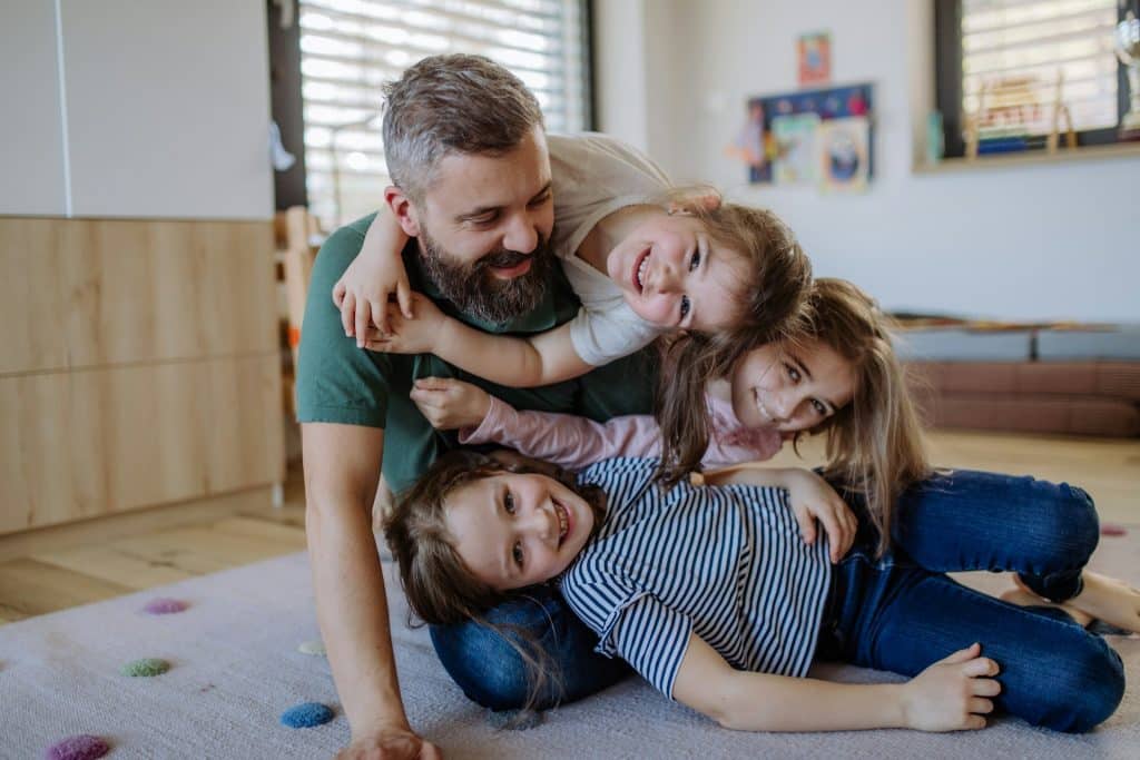 A father playing with his three daughters at home.