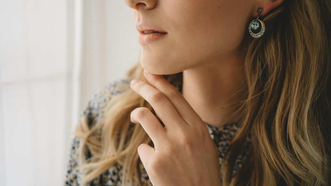 A close-up of a person touching their chin, wearing earrings and a patterned top.