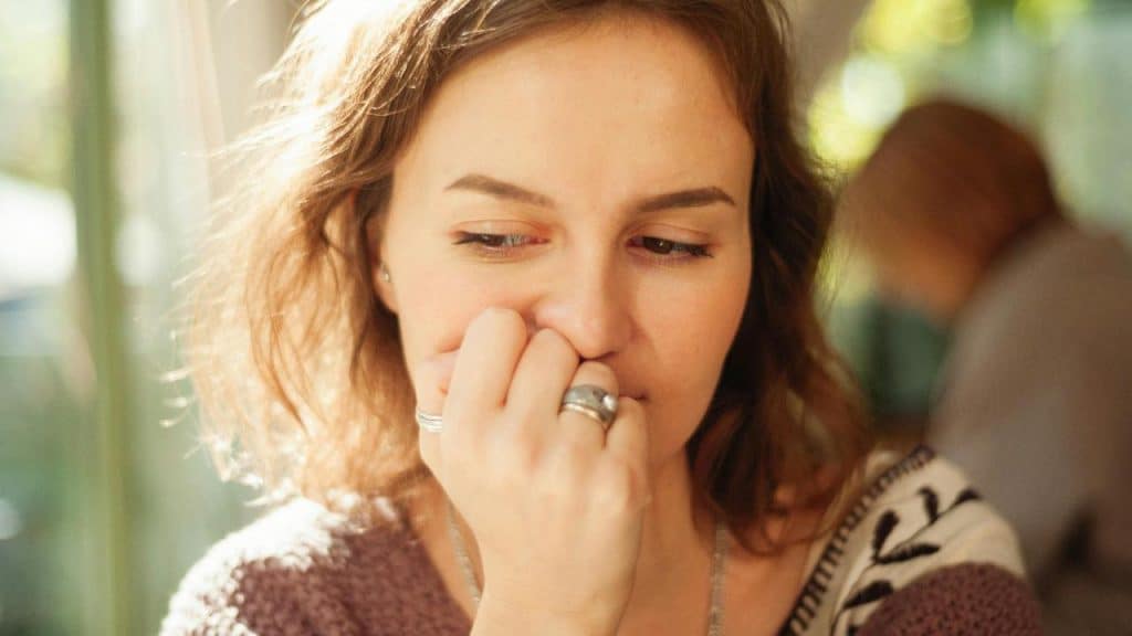 A woman with her hand near her mouth, looking downward in soft light.