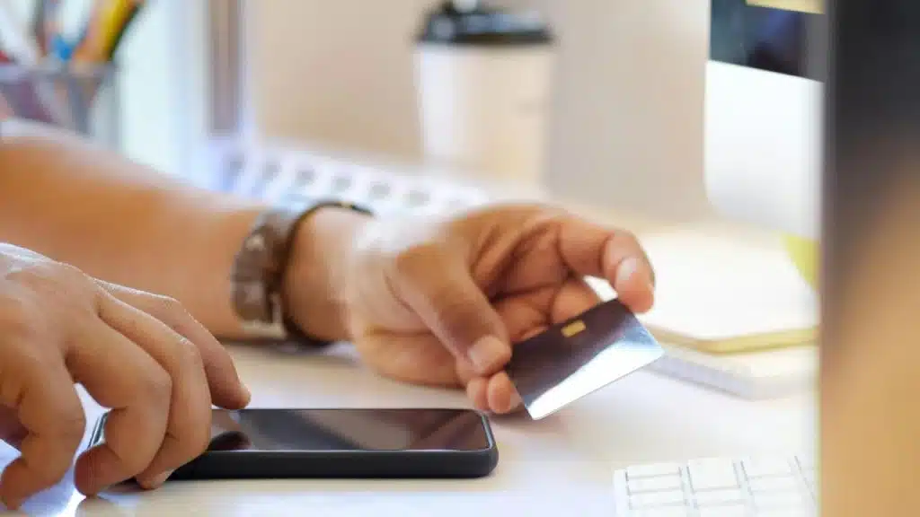 A person holding a credit card and smartphone at a desk.