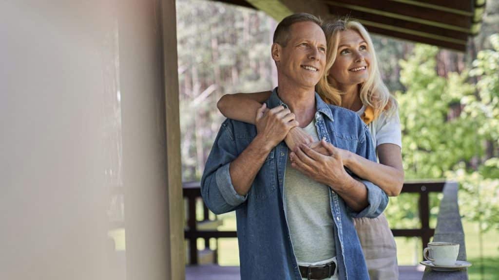 Mature couple embracing outdoors, woman has arms around man's shoulders, looking away.