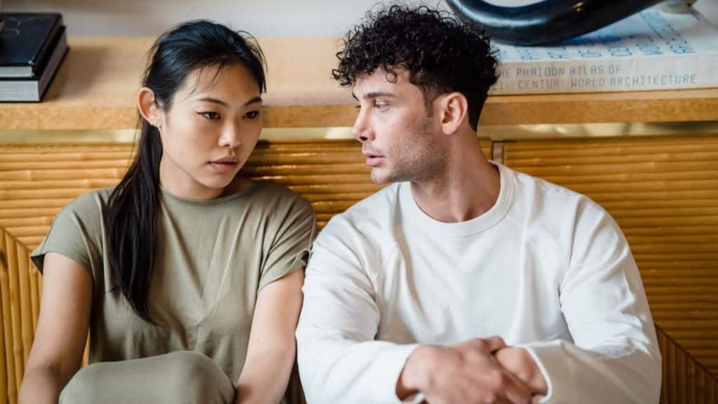 Young couple sitting together, facing each other with serious expressions indoors.