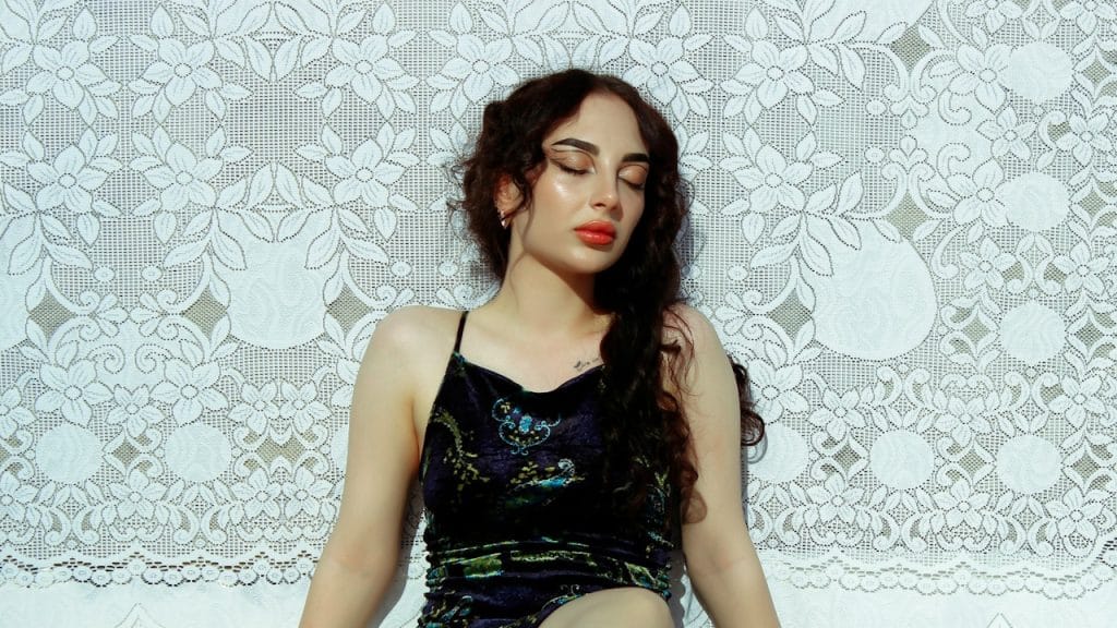 A woman wearing a black dress sitting on the floor with her legs crossed.