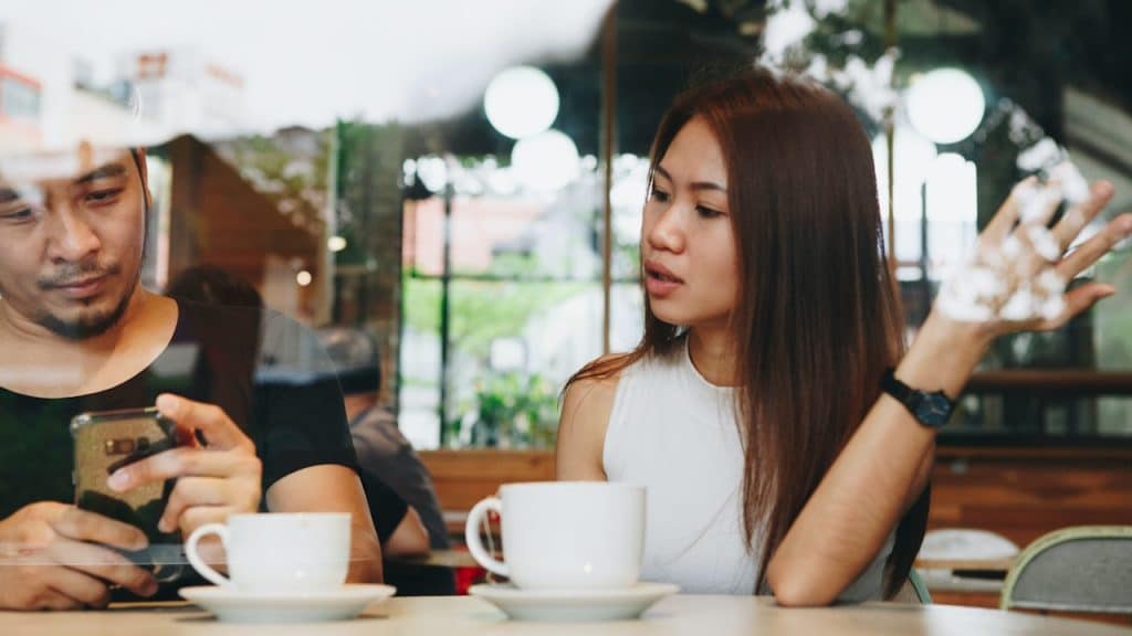 A man is focused on his smartphone while a woman next to him is talking