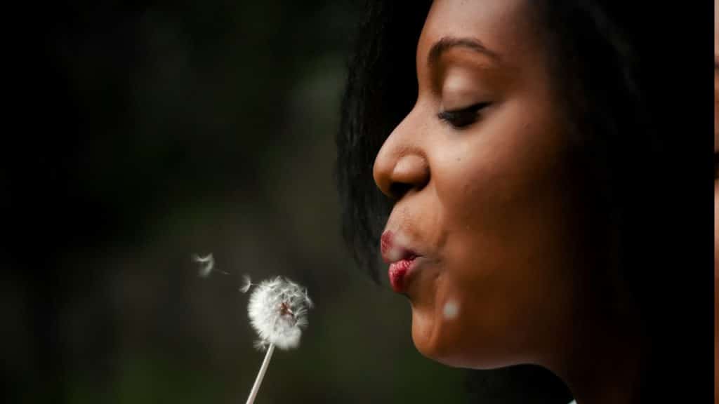 A woman in a white top blowing a dandelion.