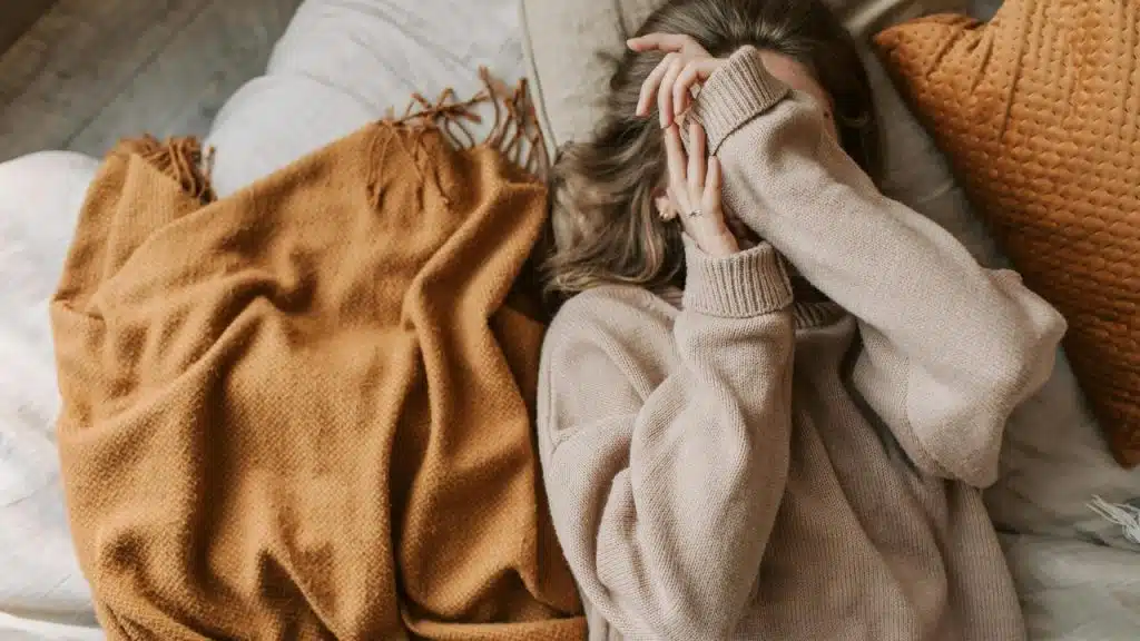 A woman lying on a bed covering her face with her hands.
