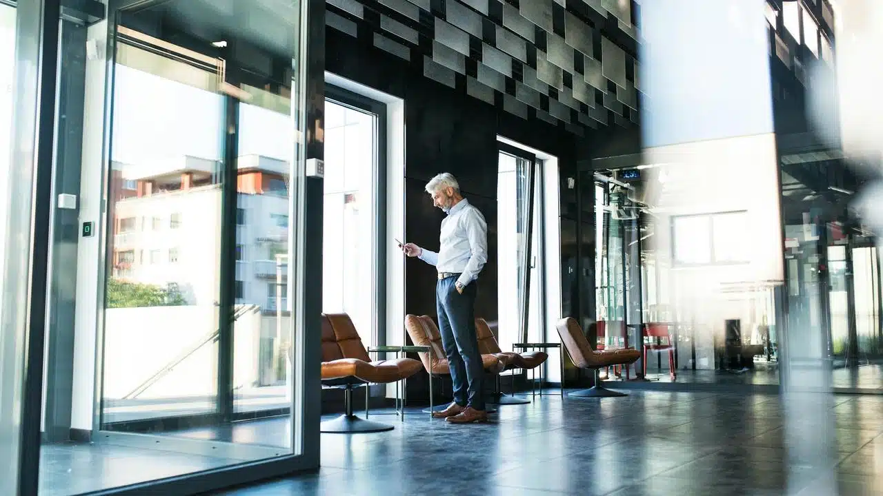 A man standing in a modern office looking at his phone.