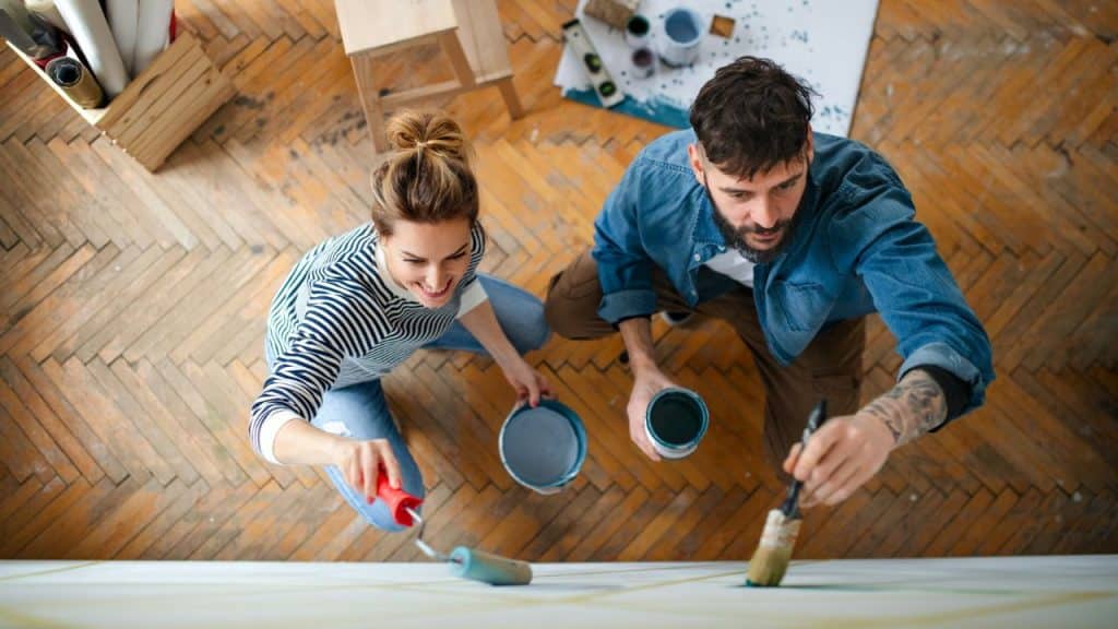 An overhead view of a man and woman painting a white wall with blue paint.