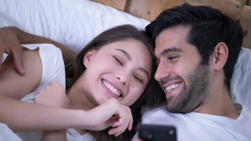A couple cuddling in bed and smiling together. 