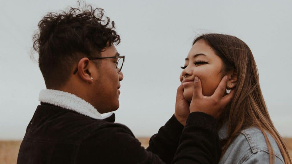 A man in a black sweater kissing a woman in a white shirt.