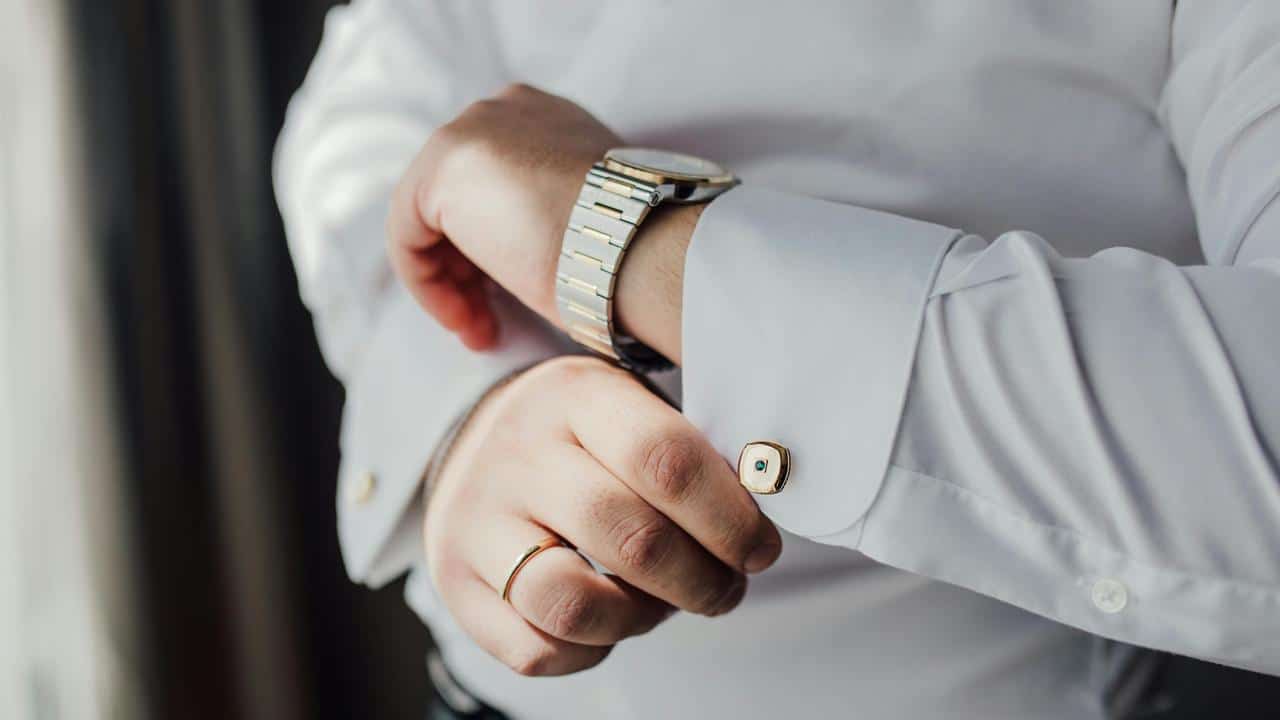 A person fastening a cufflink on a white dress shirt.