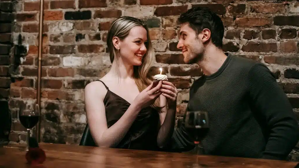 A couple smiling at each other as the woman holds a lit cupcake.