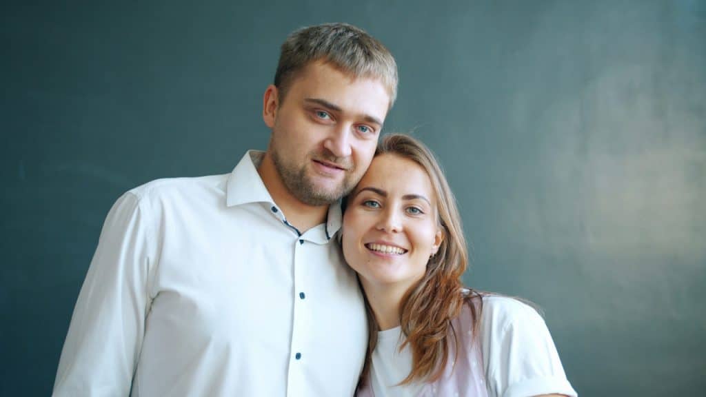 A couple smiling together against a dark background.