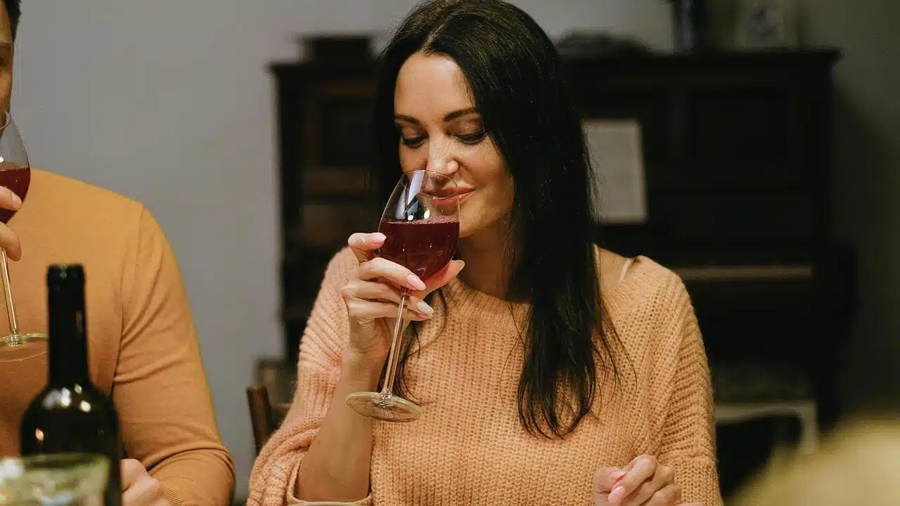 A woman smiling while holding a glass of red wine at a table.