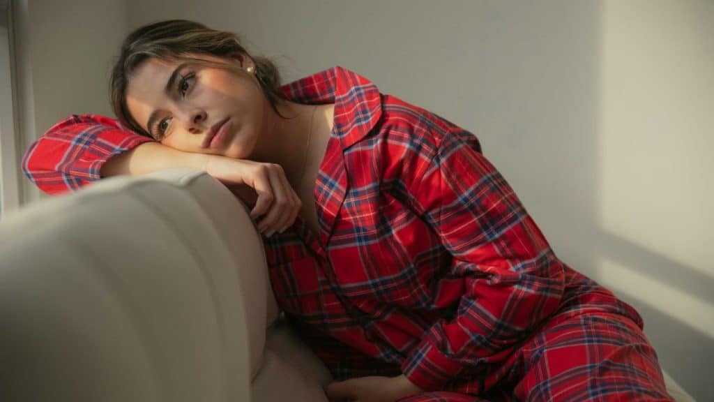 A woman in a red plaid shirt rests her head on a sofa while looking away.