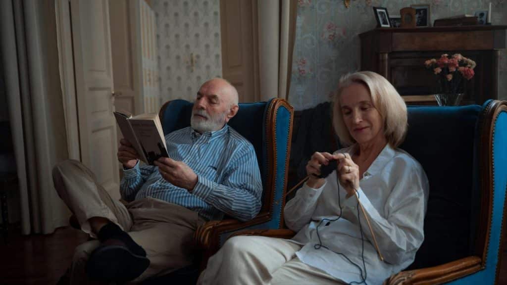 A couple sitting in armchairs, with one reading and the other knitting.