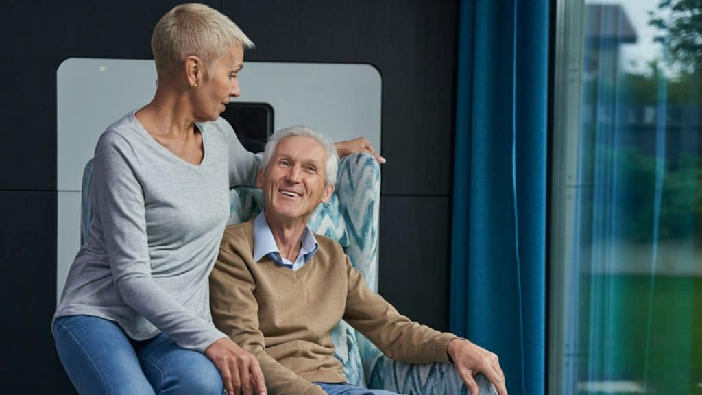 Charming woman sitting on the arm of a chair while looking at her happy man.