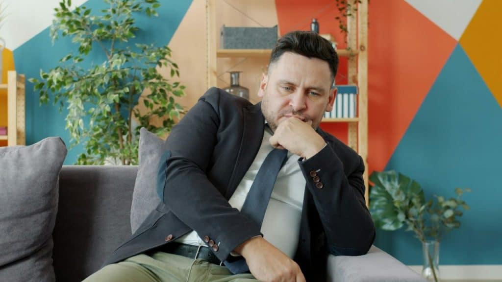 Pensive man in a suit jacket and tie sitting on a gray couch.