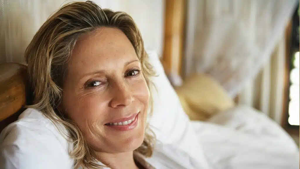 A woman lying on a bed smiling for the camera.