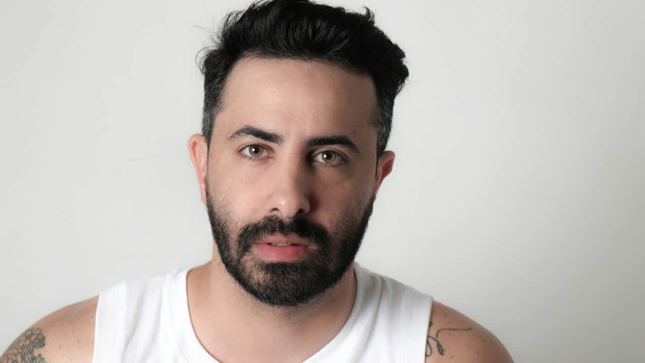 Close-up portrait of a serious bearded man in a white tank top.