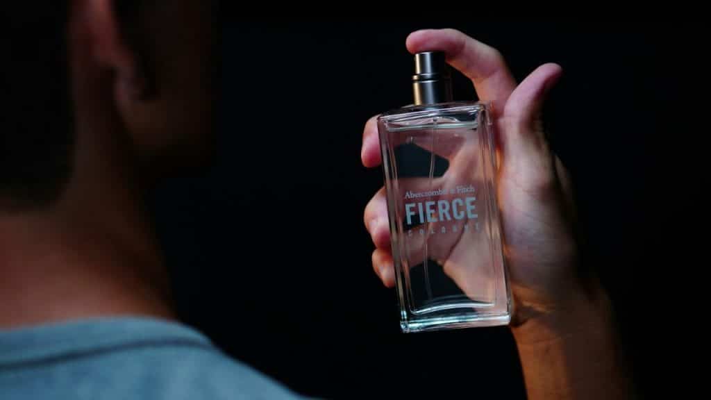 A person holds a bottle of Abercrombie & Fitch Fierce Cologne against a black background.