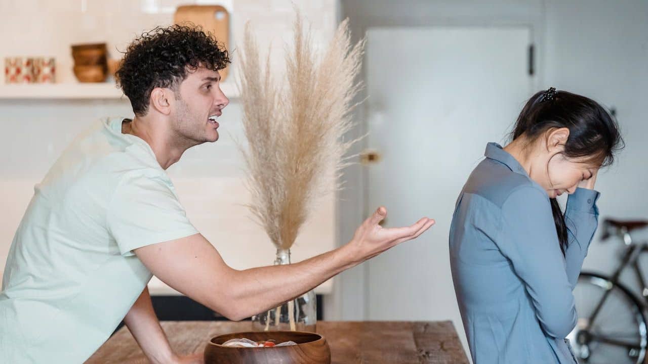 A man shouts and gestures towards a crying woman with her back turned to him.