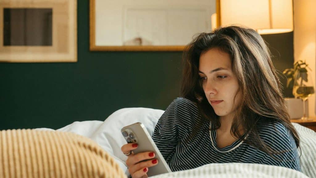 A woman lying in bed looks at her phone with a calm expression.