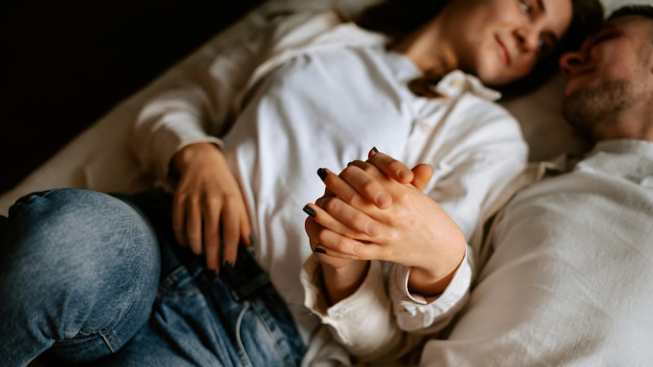 A close-up shot of a couple lying in bed, asleep and embracing each other.