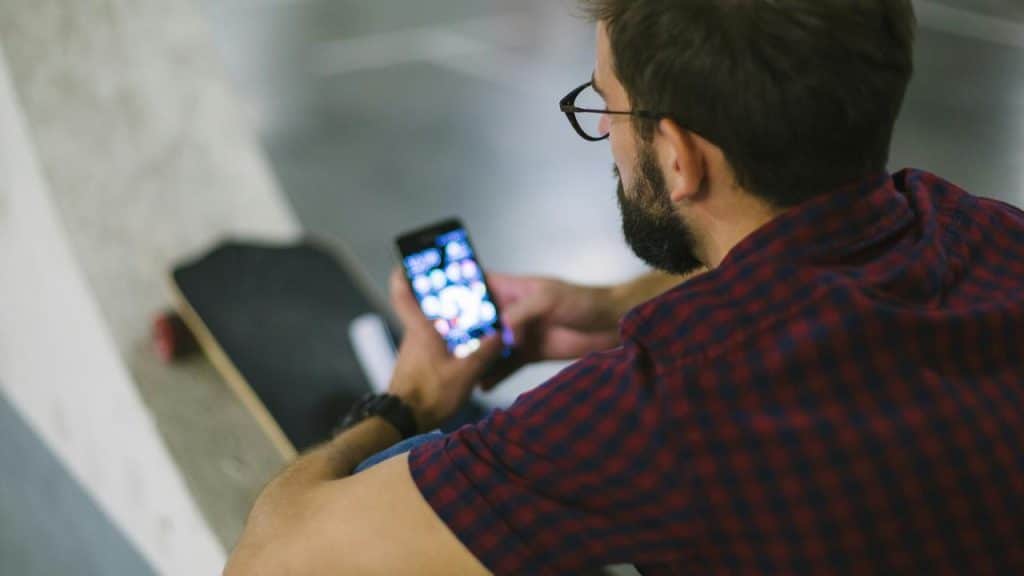 A person looking at their phone while sitting with a skateboard beside them.