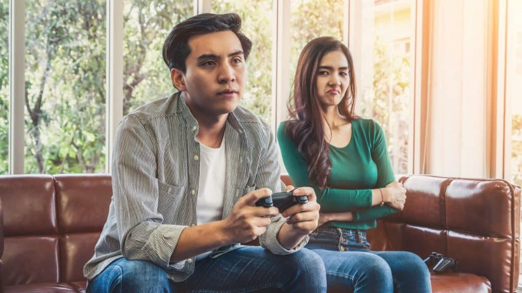 A man plays video games intensely while a woman beside him looks annoyed.