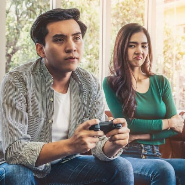 A man plays video games intensely while a woman beside him looks annoyed.