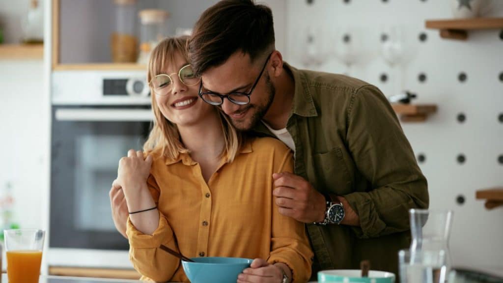 Smiling woman in glasses and man embracing in a well-lit kitchen.
