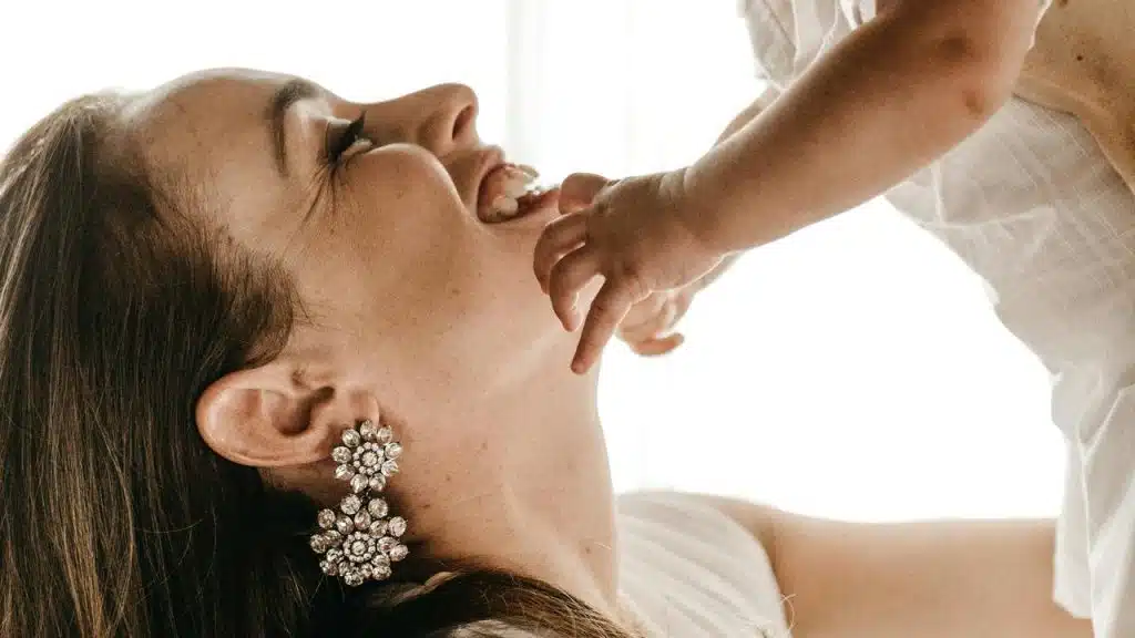 A woman wearing large earrings smiles while holding a baby who touches her face.