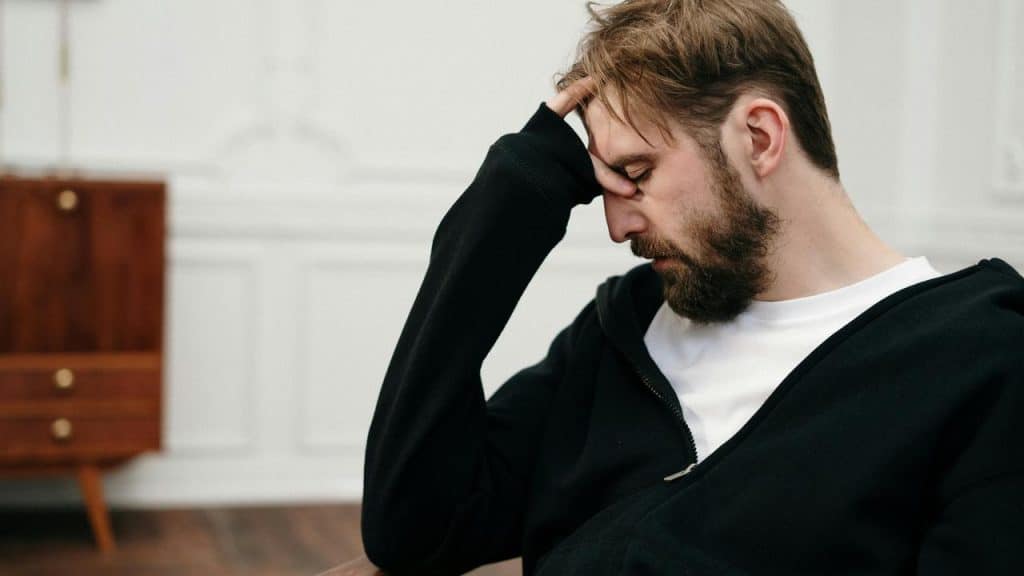 A man sitting with his hand on his forehead looking down.