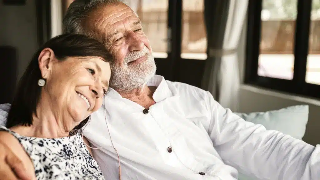 An older couple relaxing together, smiling contentedly while sitting on a couch.