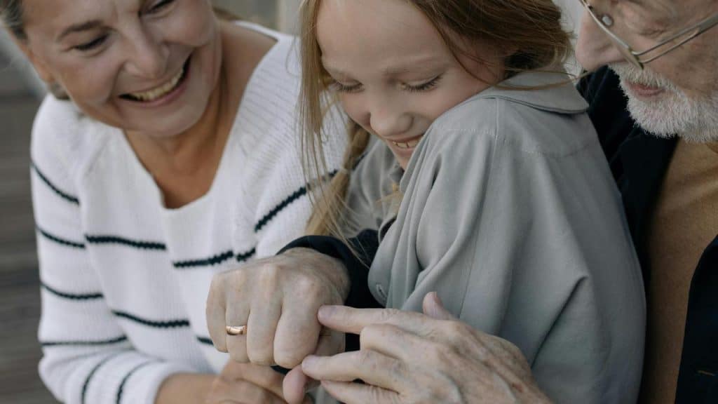 A senior couple sitting with their granddaughter, smiling and playing together.