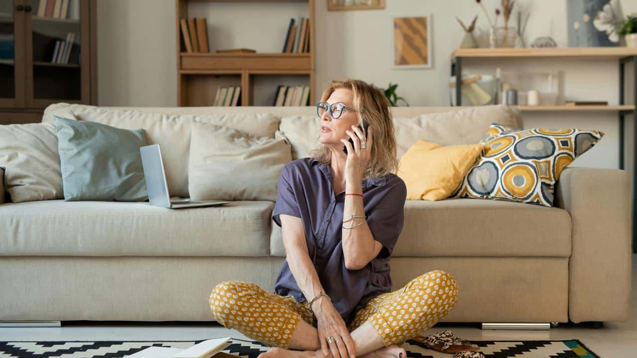 A woman sitting on the floor at home talking on the phone.