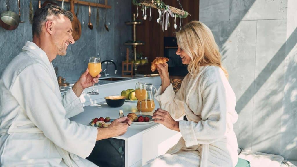 A couple in bathrobes enjoying breakfast and orange juice together.