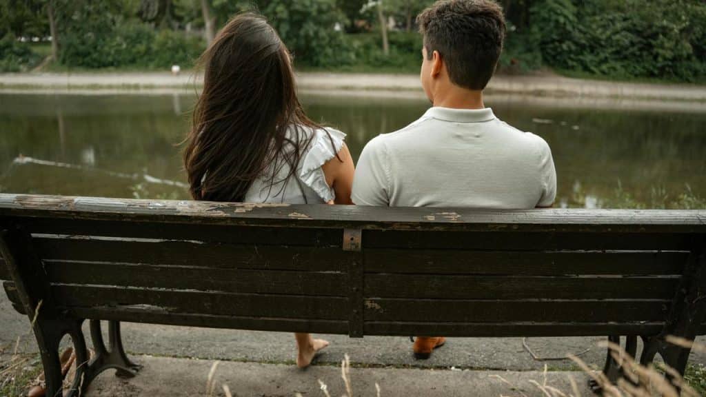 A couple sitting on a bench facing a pond.