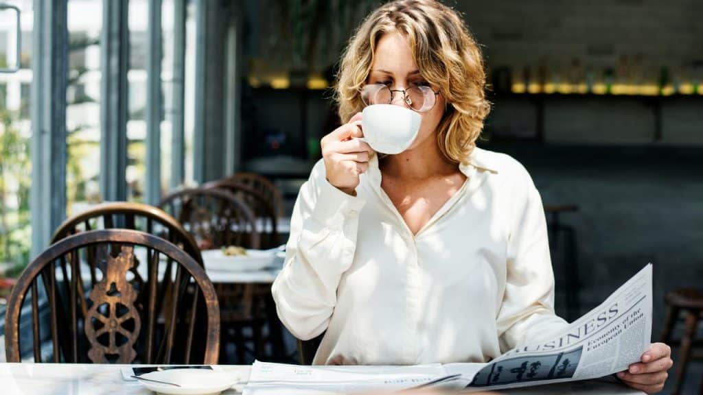 A woman drinking coffee while reading a newspaper.
