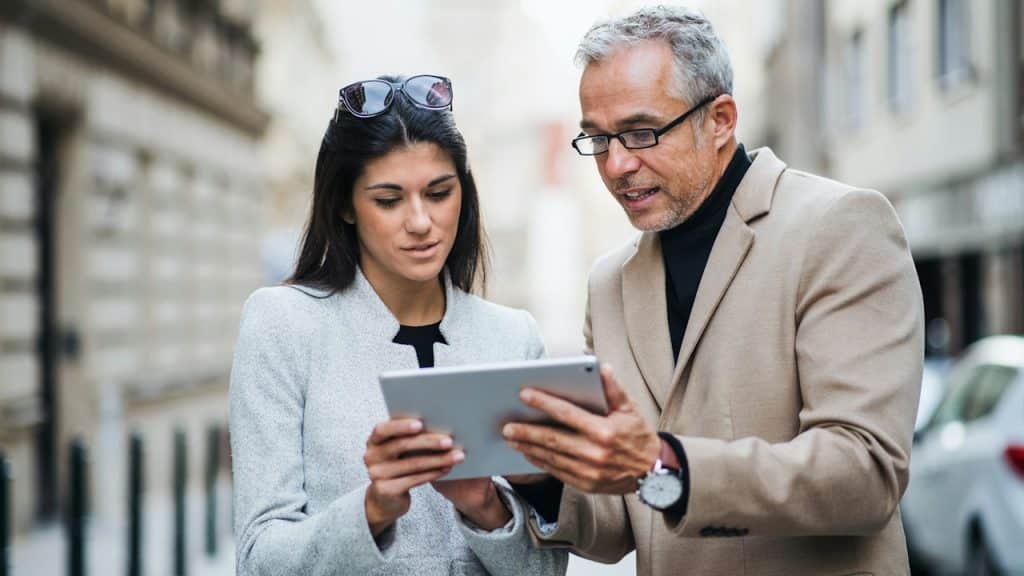 A mature man and young woman, business partners, with a tablet, standing outdoors in the city of Prague, talking