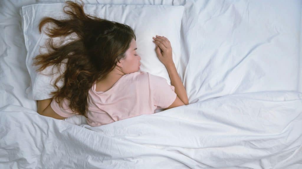 Overhead view of a woman with long hair sleeping peacefully in white bedding.