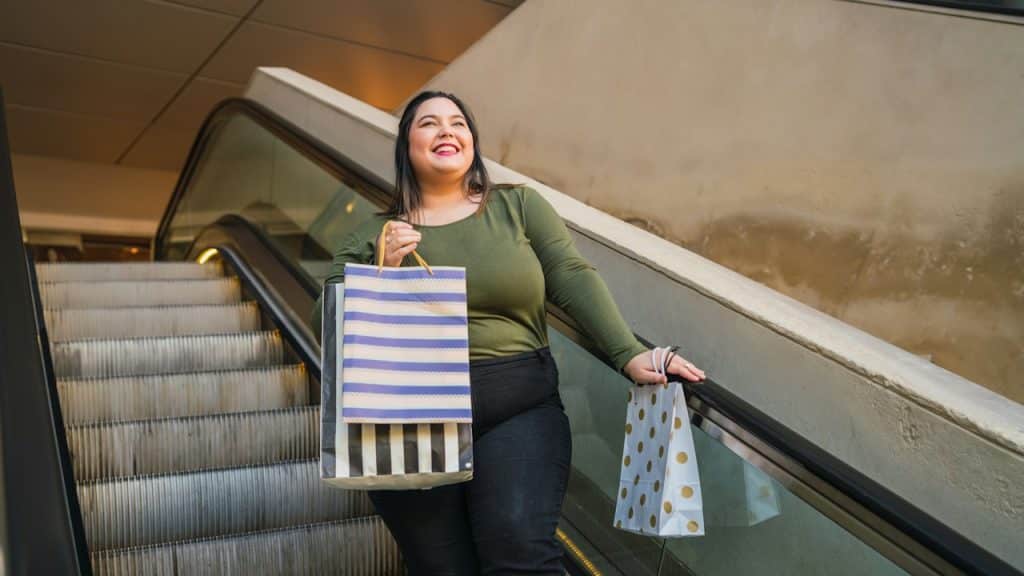 A woman smiling brightly while riding an escalator and holding several shopping bags.