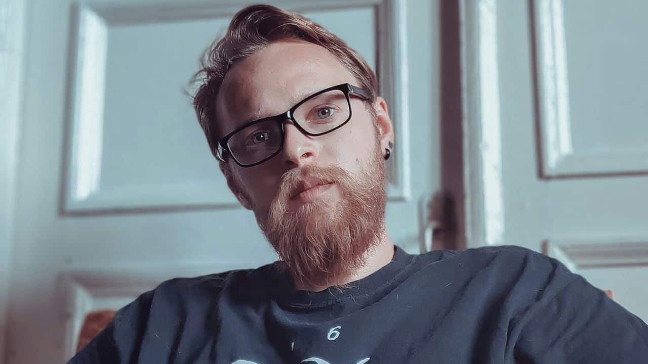 Man with red beard and black glasses looking directly at the camera.