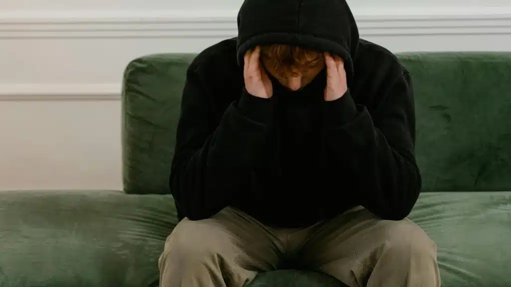 A person in a hoodie sitting on a couch with their head in their hands