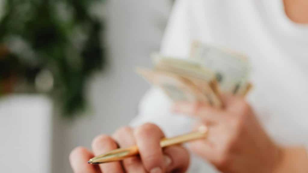 A person holding cash and a pen, counting money.