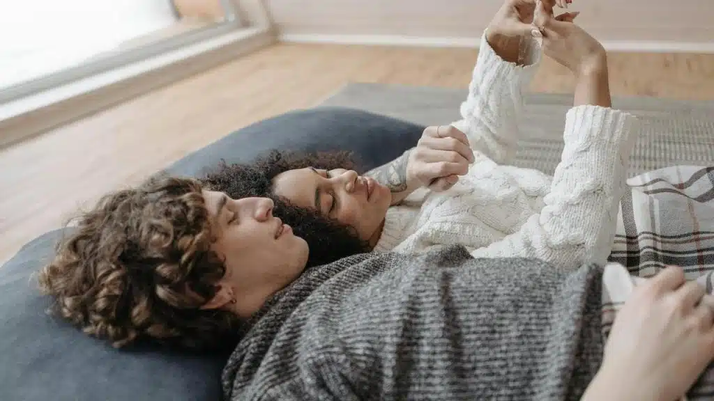 A couple lying together on a cozy blanket, holding hands.